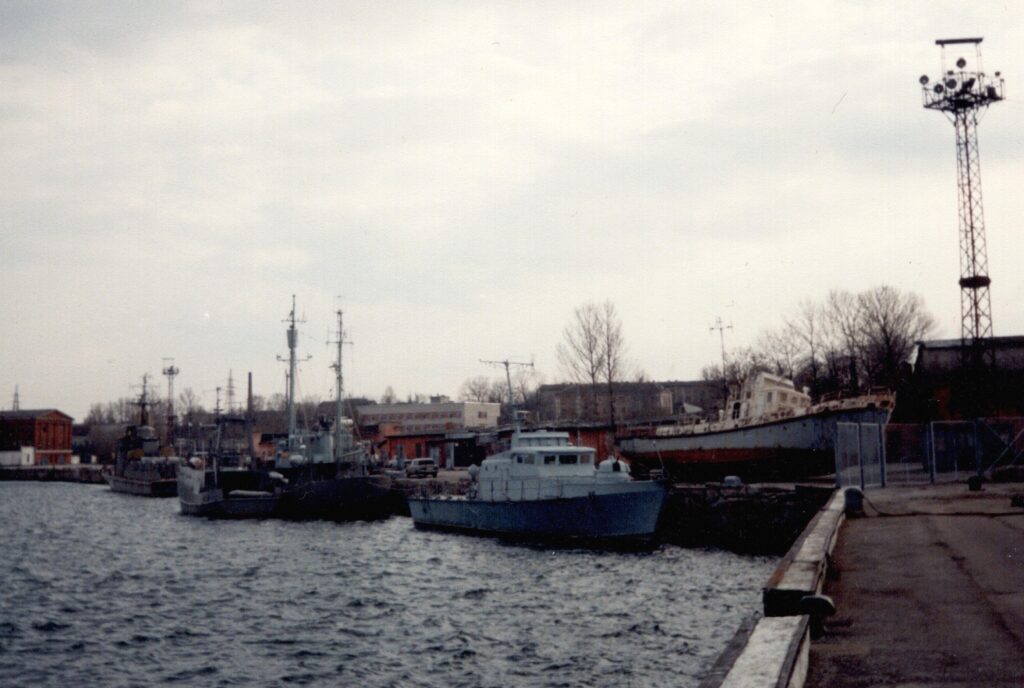 Estonian Navy vessels at Tallinn’s Mine Harbour, circa 1995. From left: a Kondor-class minesweeper, an auxiliary vessel (a former fishing ship), a Maagen-class ship, a Zhuk-class patrol boat, and a Po-2-class boat positioned on shore. Photo by Hummel15, shared under the CC BY 3.0 licence.