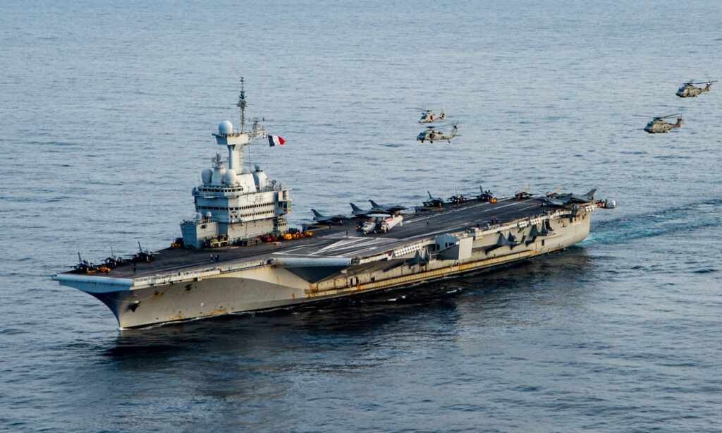 The French aircraft carrier Charles de Gaulle sails in the Ionian Sea as allied helicopters fly overhead, 17 March 2022. Public domain.