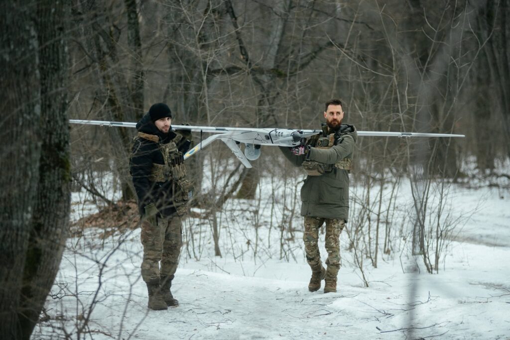 Ukrainian soldiers carry a fixed-wing drone through a snow-covered forest, underlining how unmanned aircraft have become central to modern battlefield operations. Photo by Tekever.