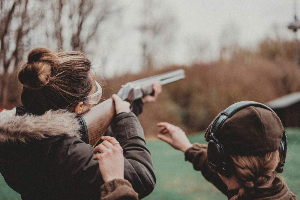 A woman takes aim at an outdoor shooting range as another participant looks on. Photo: Remy Gieling / Unsplash.