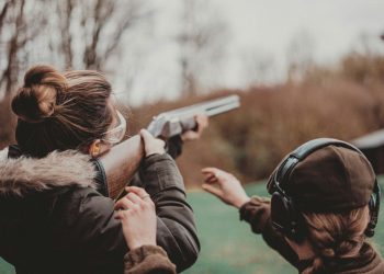 A woman takes aim at an outdoor shooting range as another participant looks on. Photo: Remy Gieling / Unsplash.