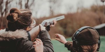 A woman takes aim at an outdoor shooting range as another participant looks on. Photo: Remy Gieling / Unsplash.
